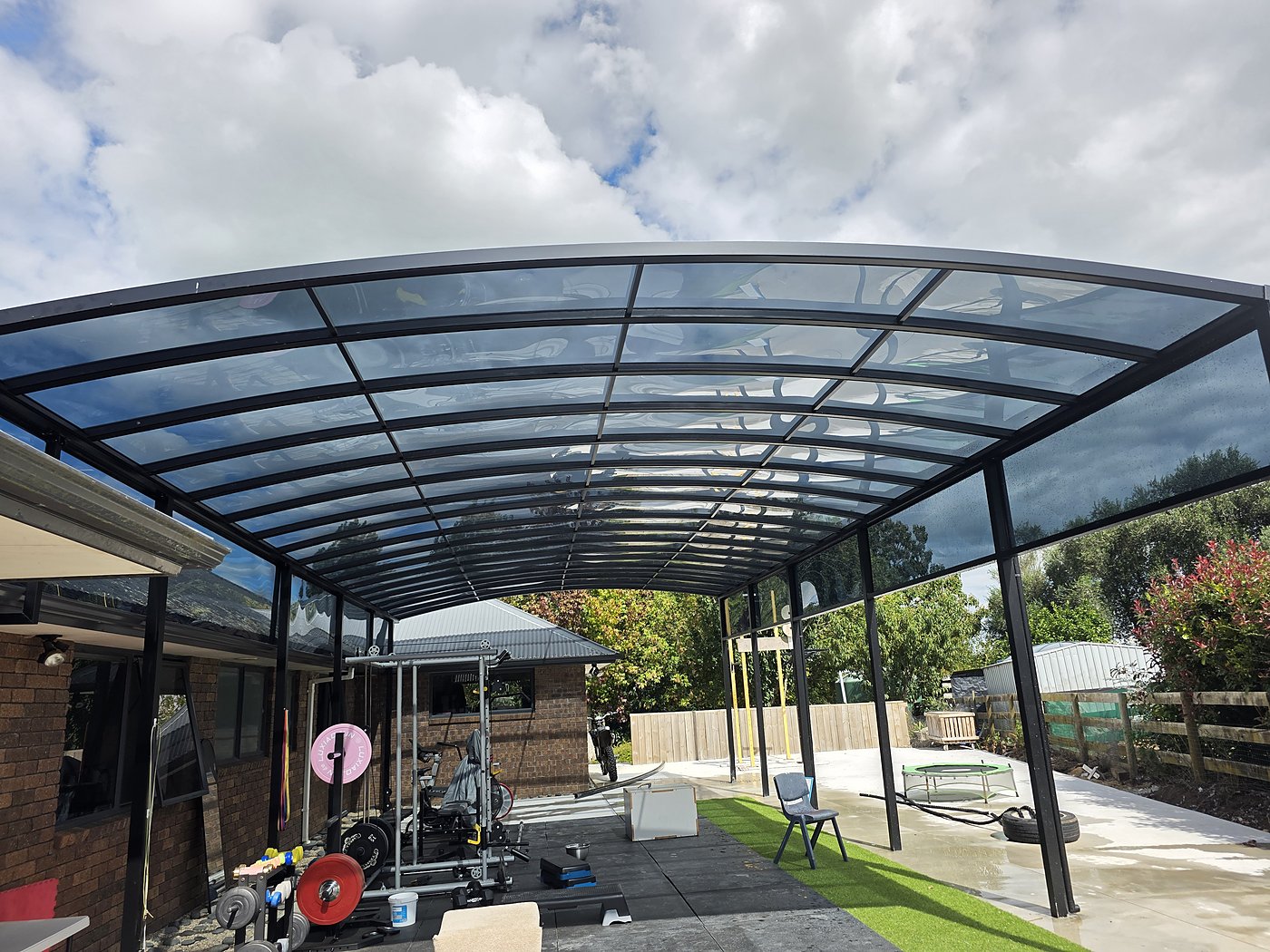 Curved glass carport over timber deck with garden view