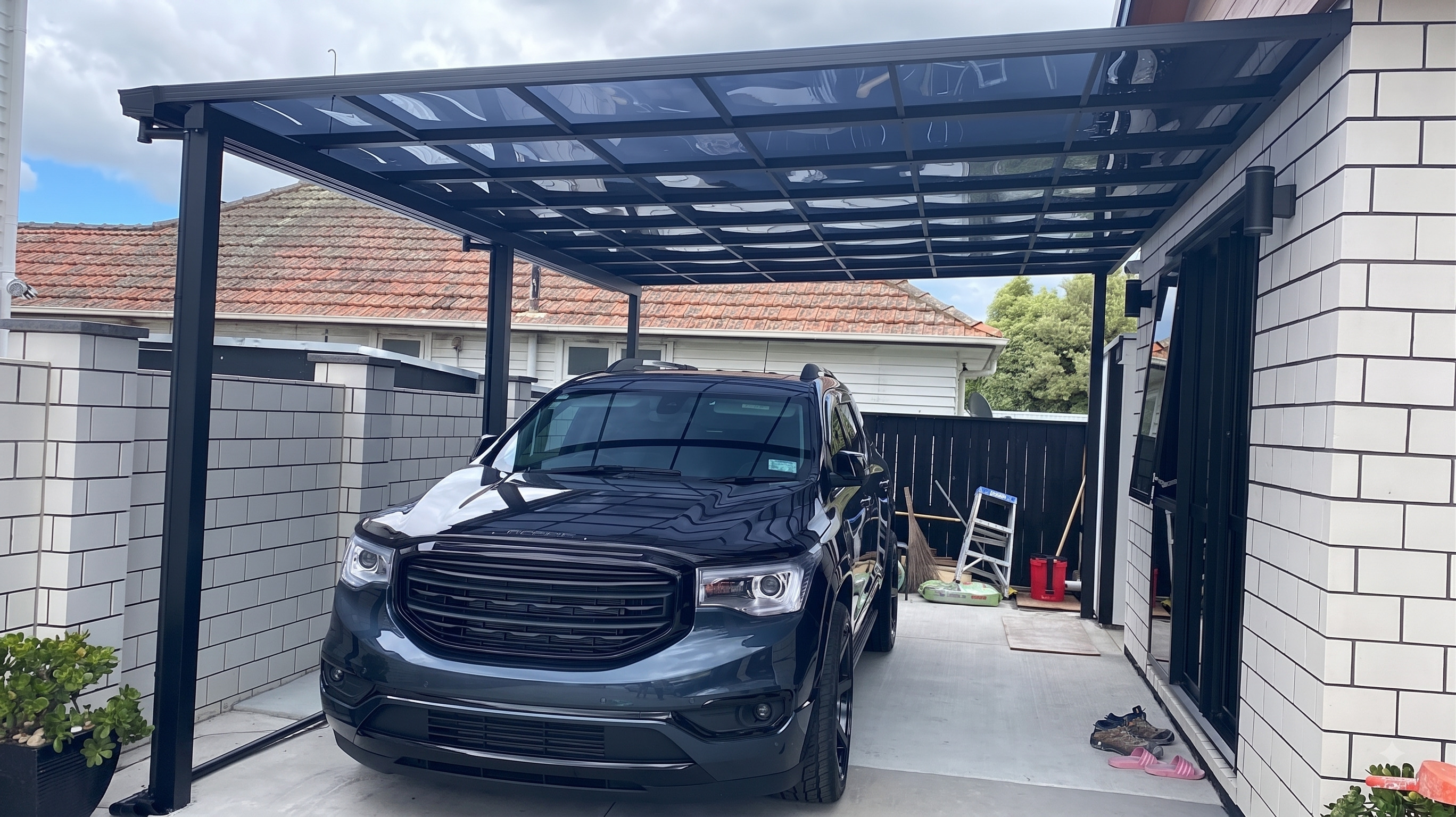 Glass carport with black SUV on white brick driveway